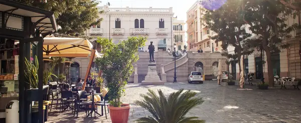 Bronze statue of Biagio Camagna in Piazza Camagna, framed by Liberty-style buildings and a semicircular staircase in Reggio Calabria.