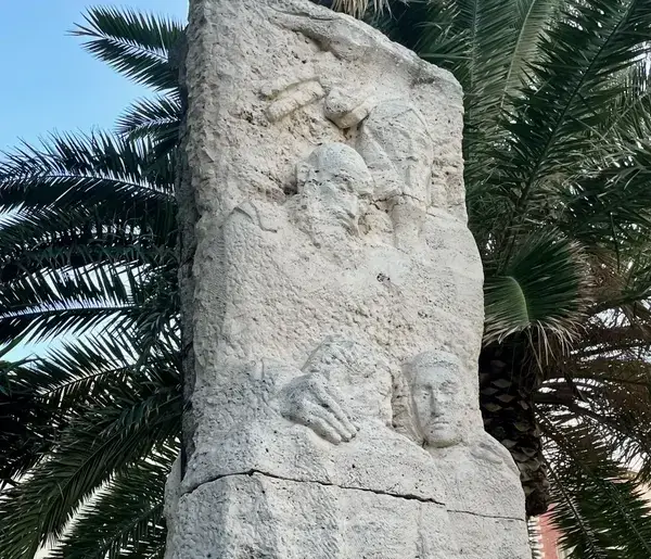 Monument to Francesco Sofia Alessio in Reggio Calabria, featuring travertine base and high-relief sculpture.
